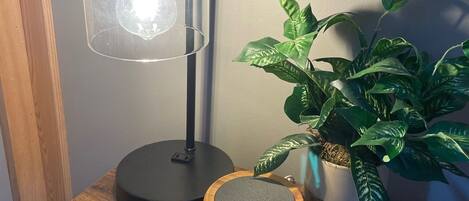 Et træbord med en skrivebordslampe, en højttaler, en potteplante og en flettede underkop.