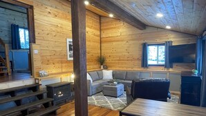 Tunnelmallinen hirsihuvilan sisustus, jossa on sohva, ruokapöytä ja takka.