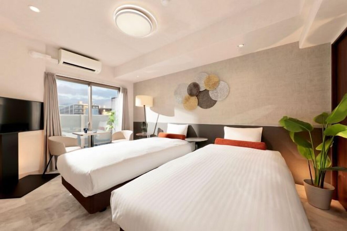 Quarto de hotel com duas camas, televisão, escrivaninha e uma janela grande.