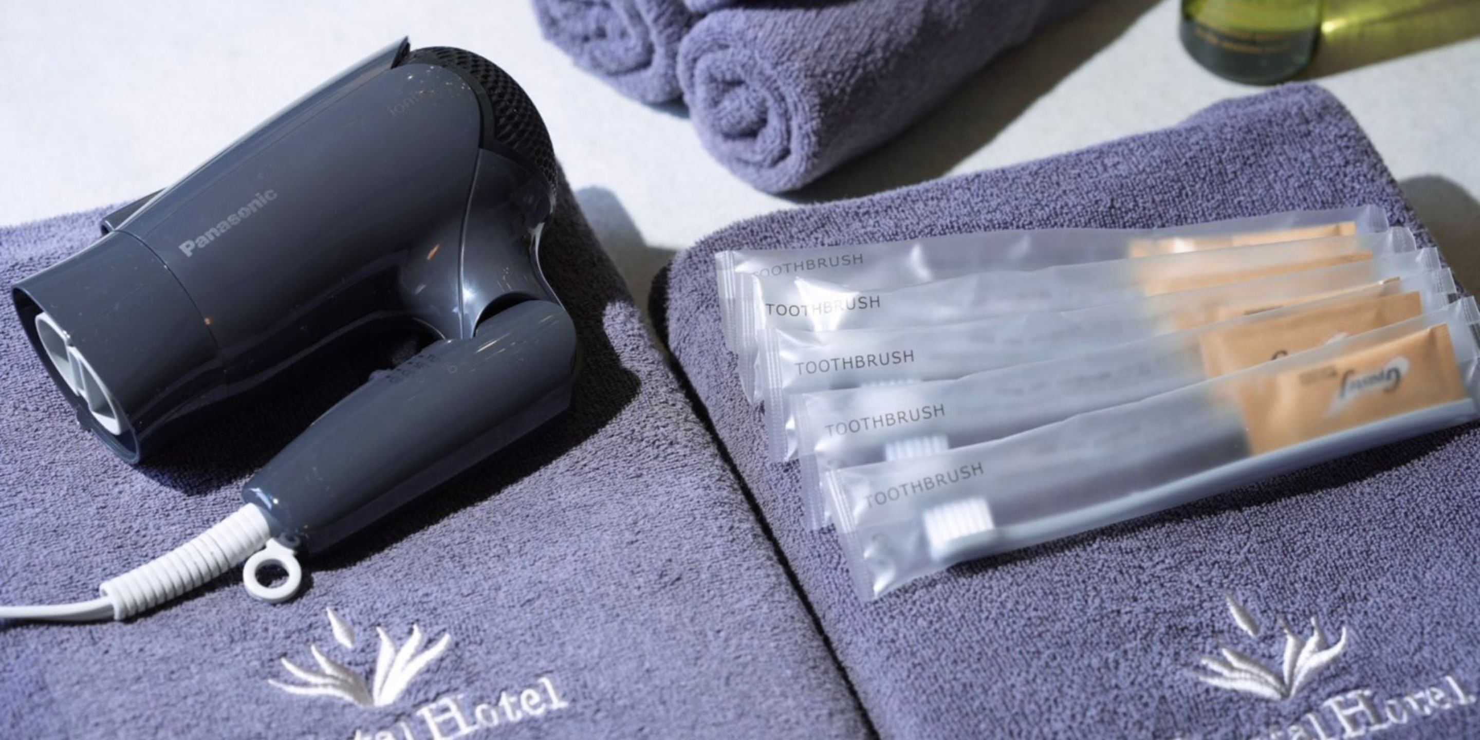 Un secador de pelo Panasonic, una toalla con el logotipo del hotel y un paquete de cepillos de dientes.