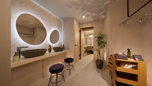 A modern bathroom with a large oval mirror, two stools, a sink with a large bowl, and a wooden vanity with a potted plant. - Doutonboricrystalhotel3 (Osaka)