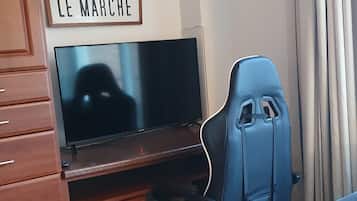 A room with a wooden desk, a television, a blue office chair, and a sign that reads 'LE MARCHÉ'.