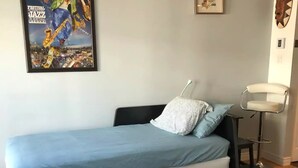 Een moderne slaapkamer met een zwart-wit gestreept matras, een blauwe sprei en een lijst met een affiche van een jazzfestival.