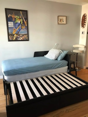 A modern bedroom with a black and white striped mattress, a blue bedspread, and a framed poster of a jazz festival.