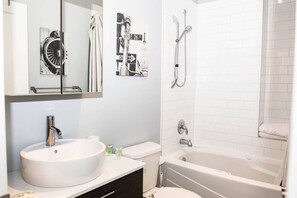 Ein modernes Badezimmer mit Waschbecken, Toilette und Badewanne in Weiß. Über dem Waschbecken hängt ein großer Spiegel, und es gibt eine Dusche mit Glastrennwand.