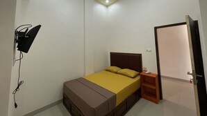A small, well-lit bedroom with a single bed, a bedside table, a wall-mounted TV, and a door leading to another room. - OYO 93414 Wisma Ratu Syariah Near SMP Negeri 2 Watang Pulu (Watang Pulu)