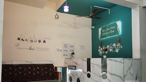 Un área de recepción con una pared color verde azulado, un mostrador de recepción y un tablón de anuncios con fotografías de viajes.