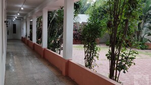 Un corredor cubierto con piso de baldosas y una fila de columnas, que conduce a un espacio exterior con plantas en macetas y árboles.