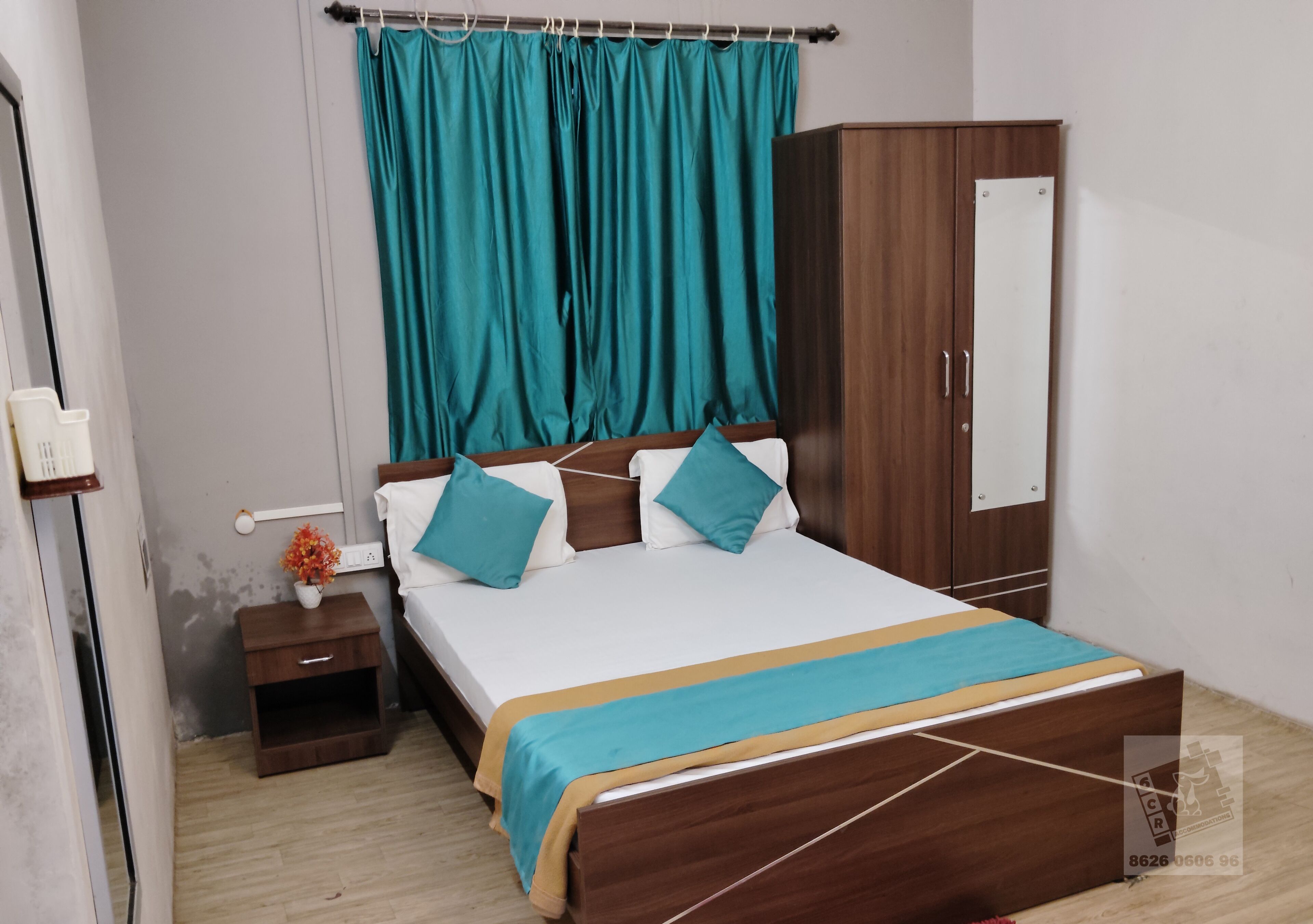 A bedroom with a wooden bed, teal curtains, a nightstand with a flower, and a wardrobe.