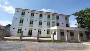 Un immeuble à plusieurs étages, doté d’une façade verte et blanche, d’une entrée sécurisée par un portail et d’une allée gravillonnée.
