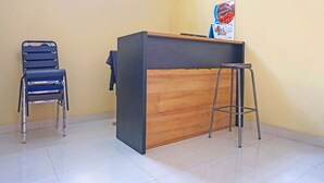 Un comptoir d’accueil avec un panneau en bois et un panneau foncé, une chaise en métal et un tabouret en métal.