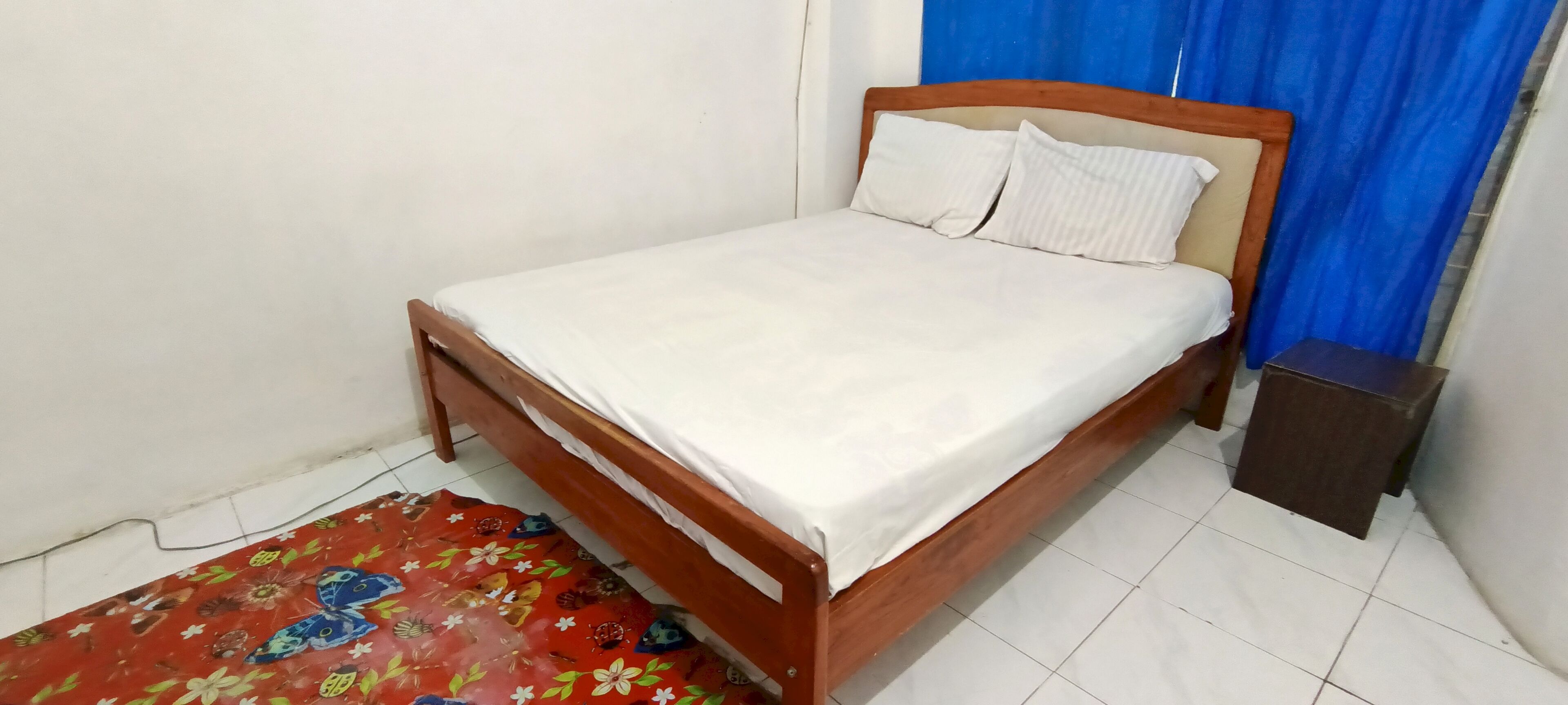 A single bed with a wooden frame and white bedding in a room with white walls and a blue curtain.