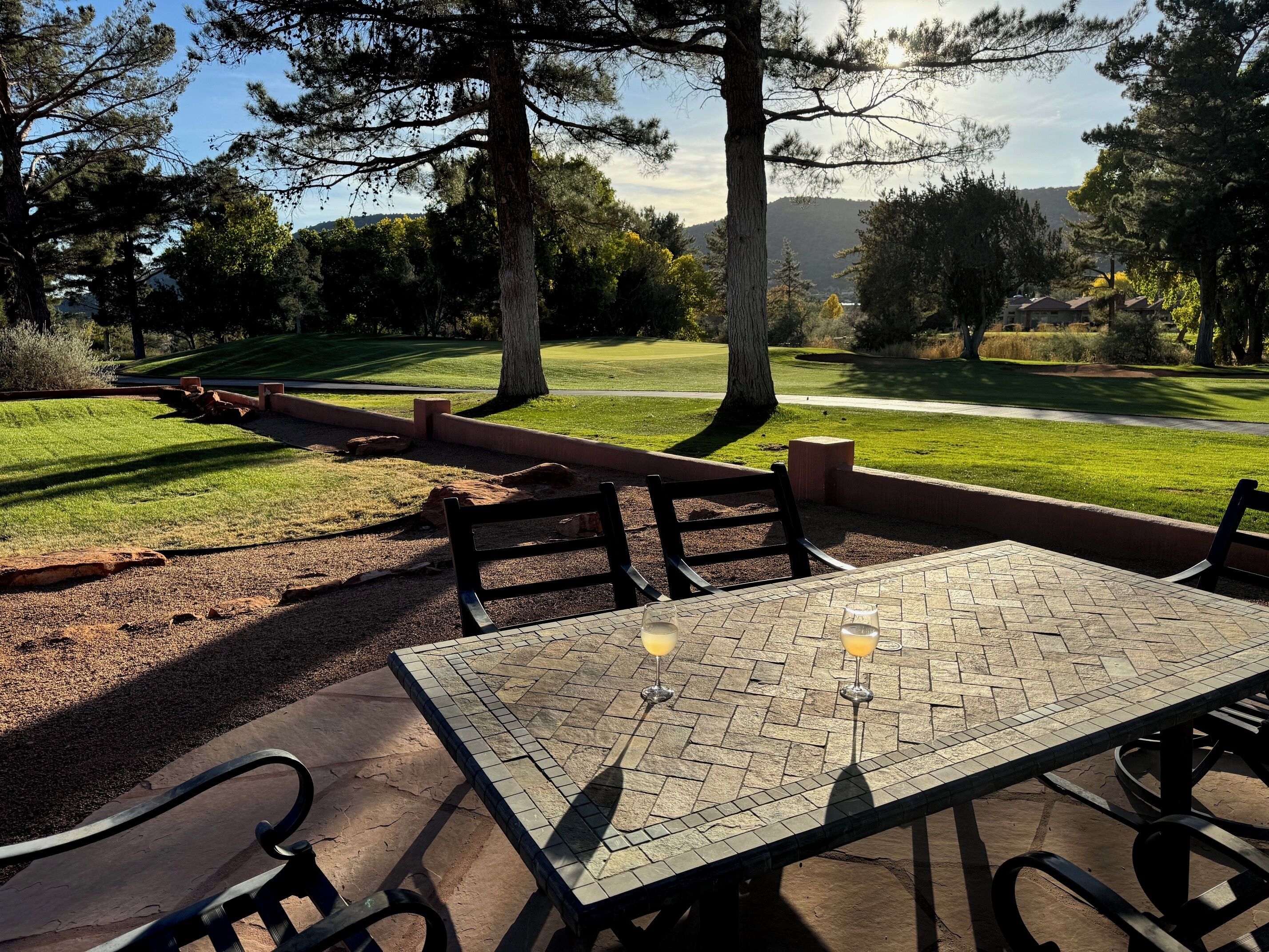 Un espace extérieur aménagé avec des tables et des bancs carrelés, entouré d’arbres et offrant une vue sur un terrain de golf.