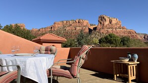 Eine Terrasse mit Tisch für zwei Personen, Stühlen und einem kleinen Tisch mit Dekoration. Im Hintergrund ist ein Gebirge zu sehen.