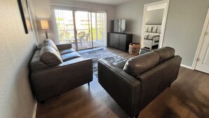 Una sala de estar con un sofá, un televisor, un mueble y un ventanal corredizo hacia el exterior.