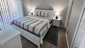 Un dormitorio con cama, mesitas de noche, un escritorio y una ventana con persianas.