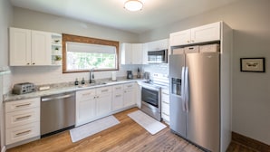 A modern kitchen with white cabinets, stainless steel appliances, and a wooden floor.