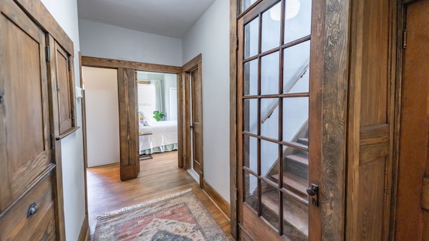 A hallway with wooden doors, a patterned rug, and a staircase leading to another room.