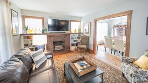 A living room with a leather sofa, a coffee table, a fireplace, a TV, and a dining area with chairs.