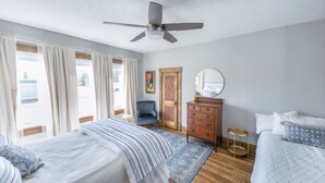 A bedroom with two beds, a ceiling fan, a dresser, a chair, and a small round table.