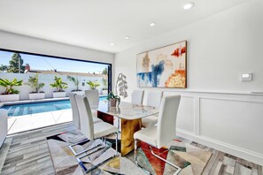 Enjoy a view of the swimming pool from the large window in this room, which features a glass table and white chairs.