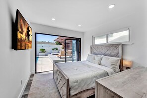 Relax in this serene bedroom with a large bed, wall-mounted TV, and sliding door to a patio area with pool and seating.