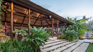 A covered outdoor area with stone steps leading to a seating area, surrounded by lush greenery. - Villa Nusantara  (Denpasar)