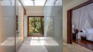 A modern hotel room with a glass door leading to a balcony, a bed with white bedding, and a ceiling light fixture. - Villa Nusantara  (Denpasar)