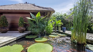 A koi pond with lily pads and a thatched-roof building. - Villa Nusantara  (Denpasar)