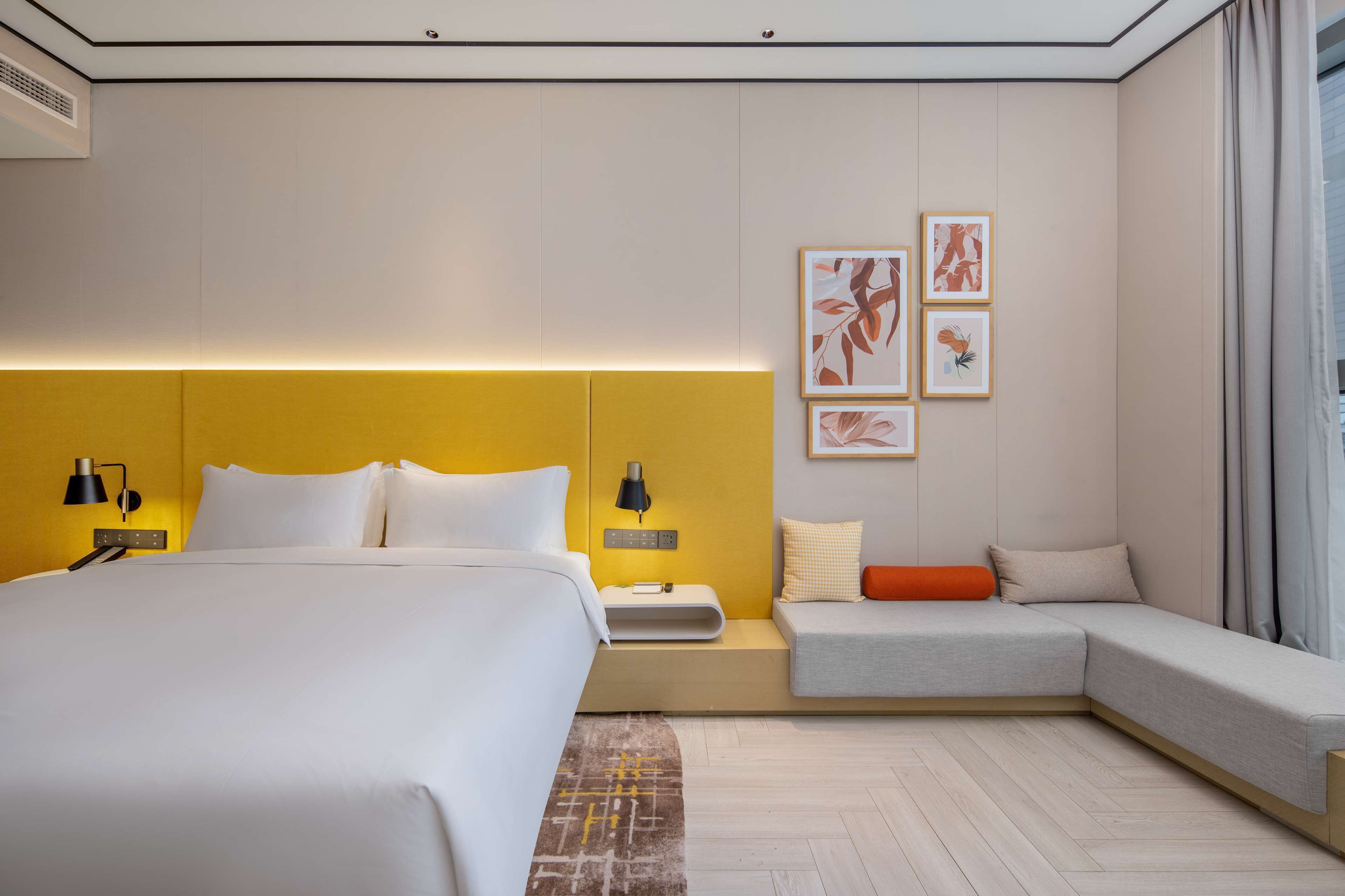 A modern hotel room with a large bed, bedside tables, a sofa, and artwork on the wall.