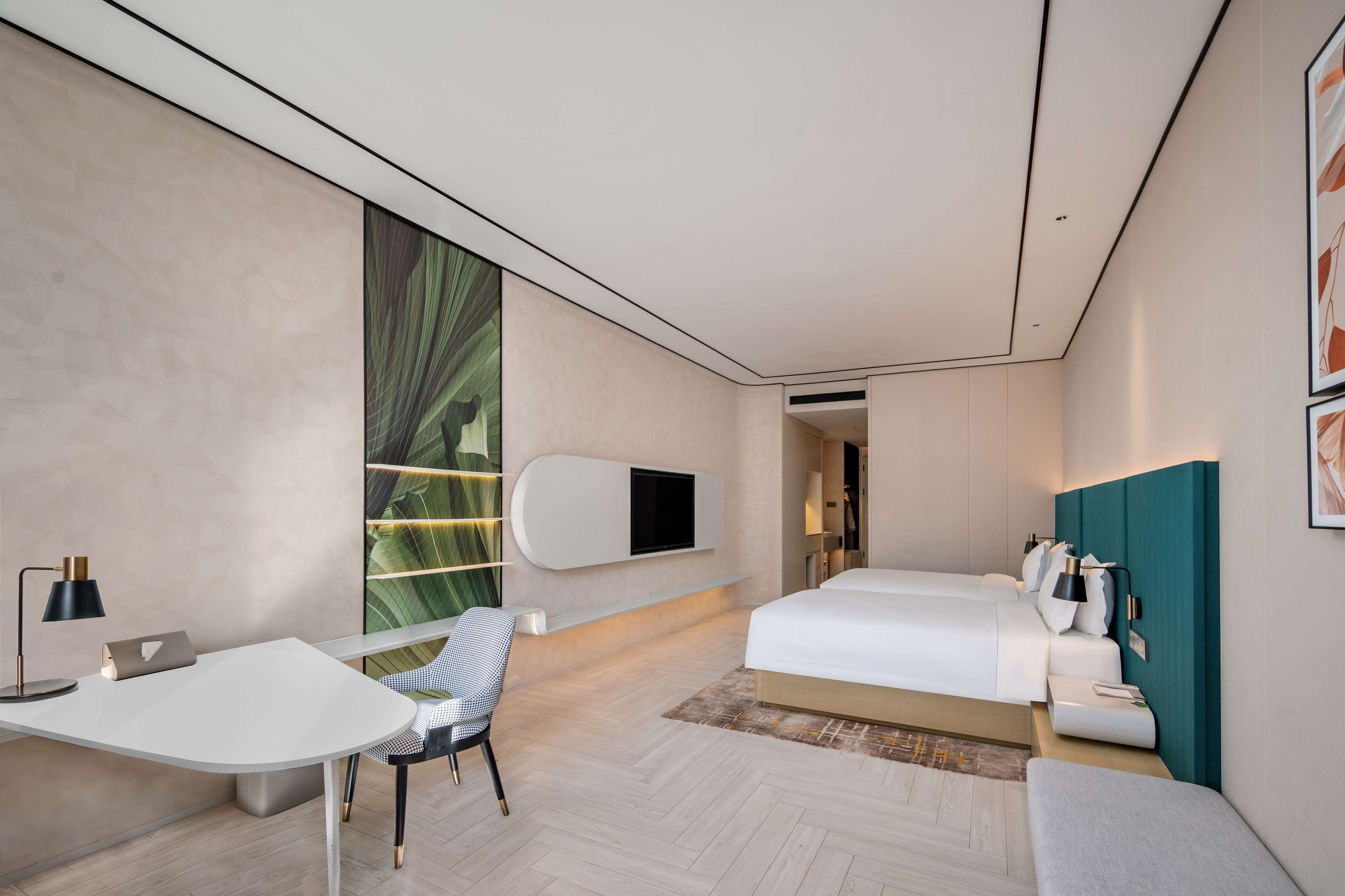 A modern hotel room with a bed, a desk, a chair, and a TV mounted on the wall.