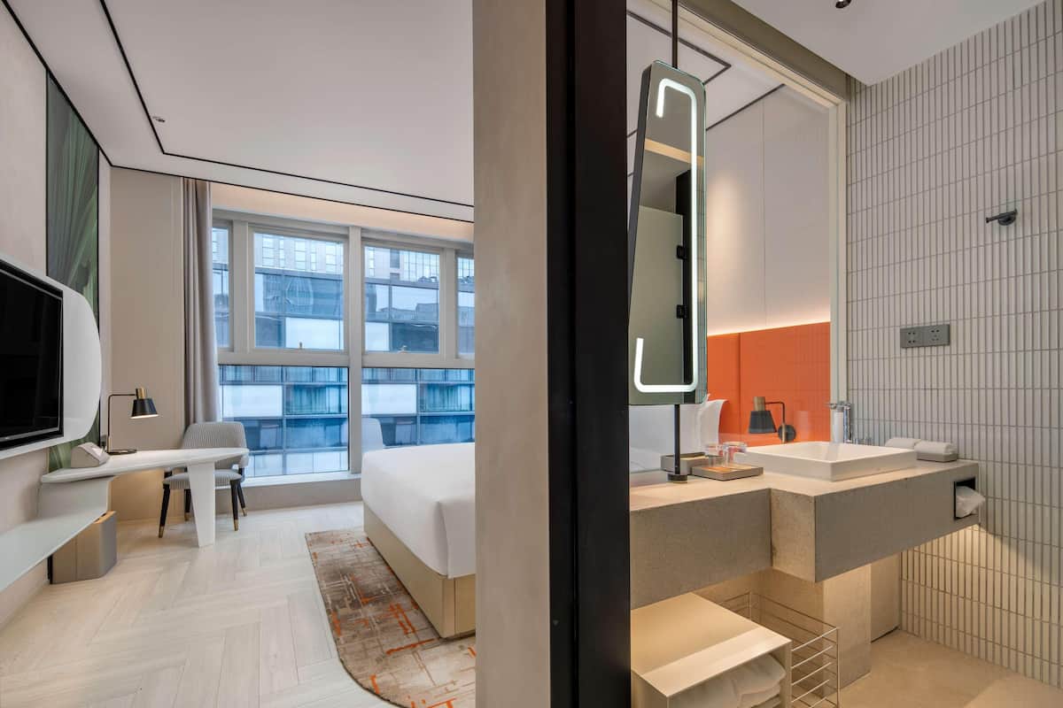Une chambre d’hôtel moderne, équipée d’un lit, d’un bureau et d’une grande fenêtre.