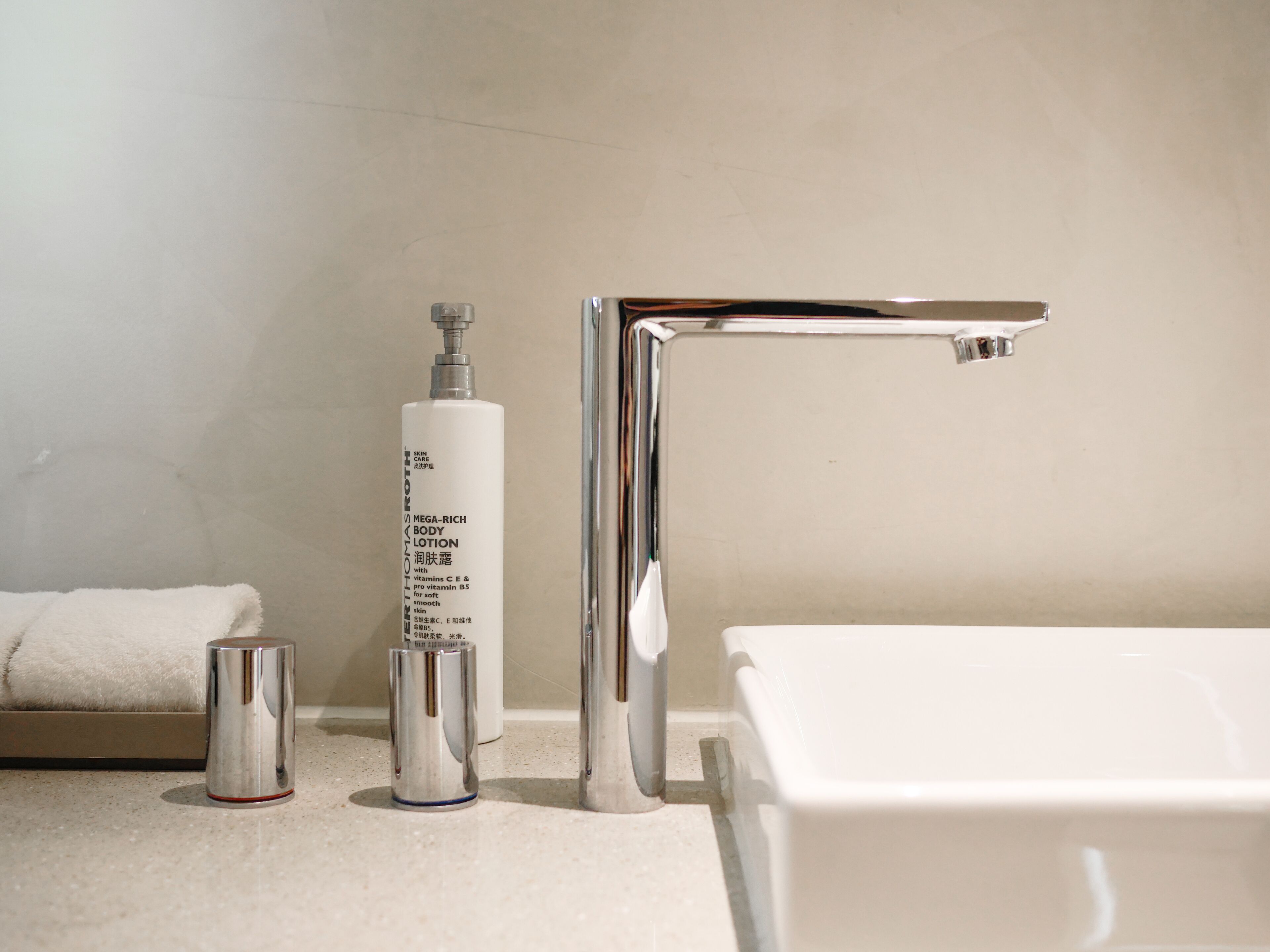A bathroom with a white sink, chrome faucet, and a bottle of lotion.