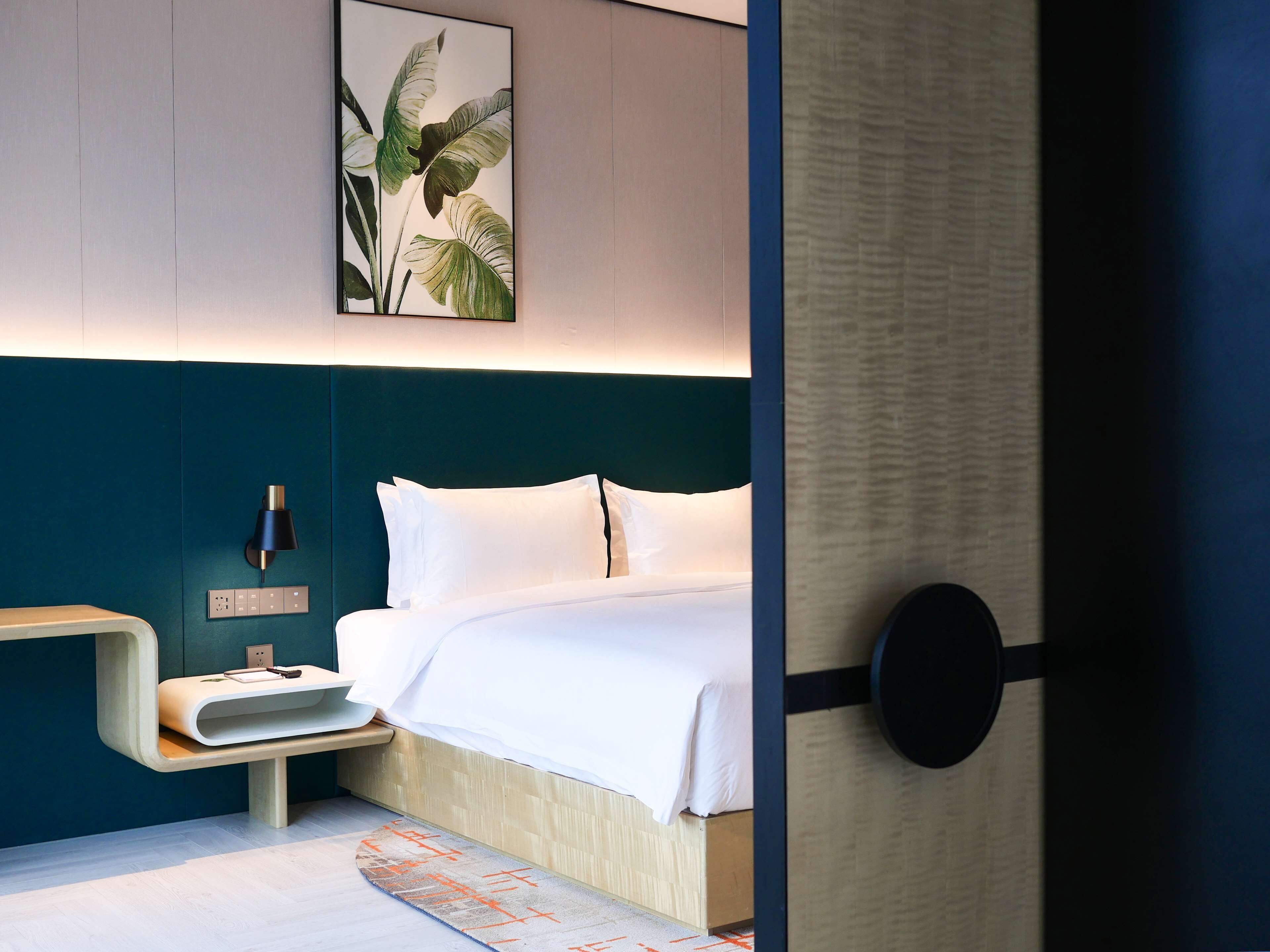 Una camera d'albergo moderna con un letto, un comodino, una lampada e un quadro appeso al muro.