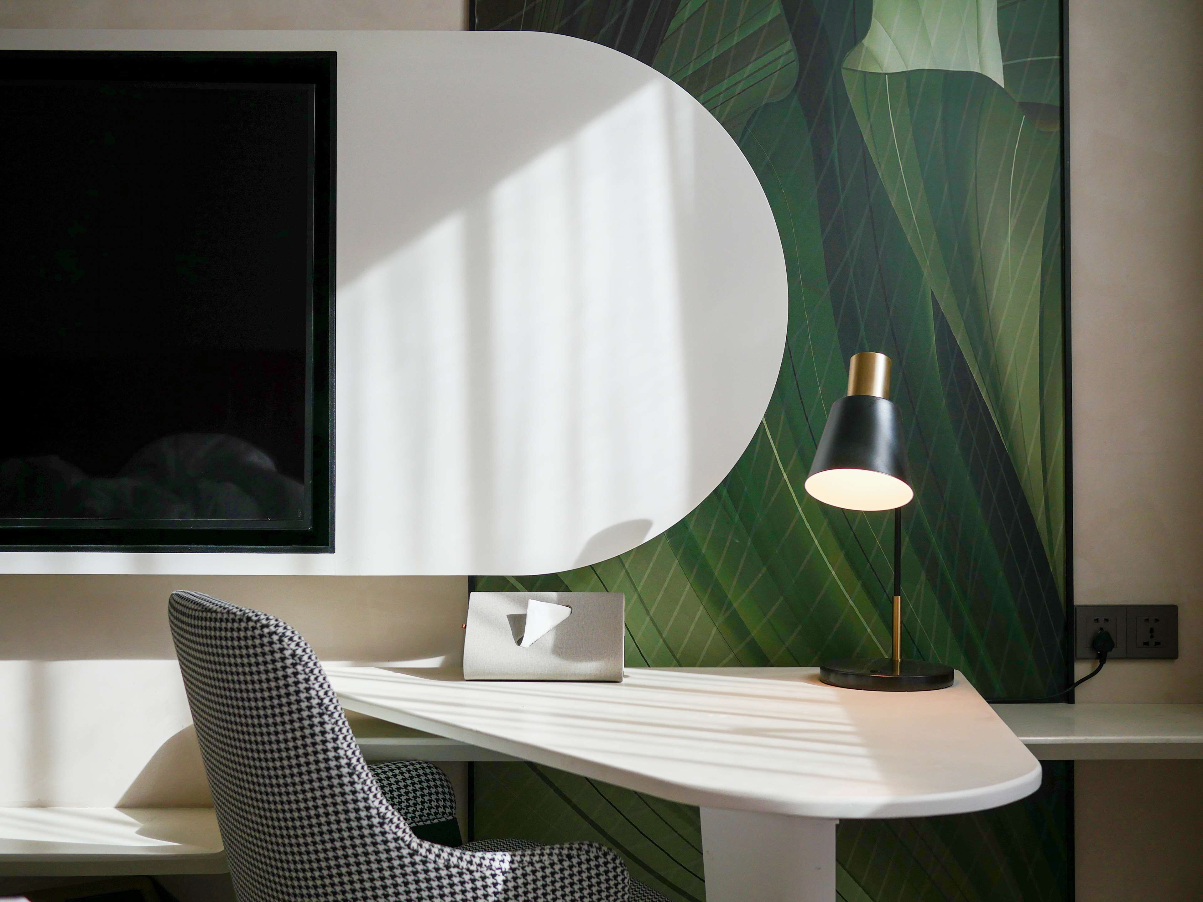 Una habitación moderna con una mesa blanca curvada, una silla a cuadros blanco y negro estilo pied de poule, una lámpara negra y un cuadro abstracto grande en la pared.