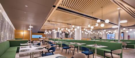 A modern dining area with green booths and tables, overhead wooden slats, and pendant lighting.