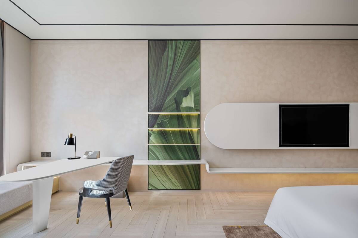 Une chambre d’hôtel moderne avec un bureau blanc, une chaise, un lit et un téléviseur fixé au mur.