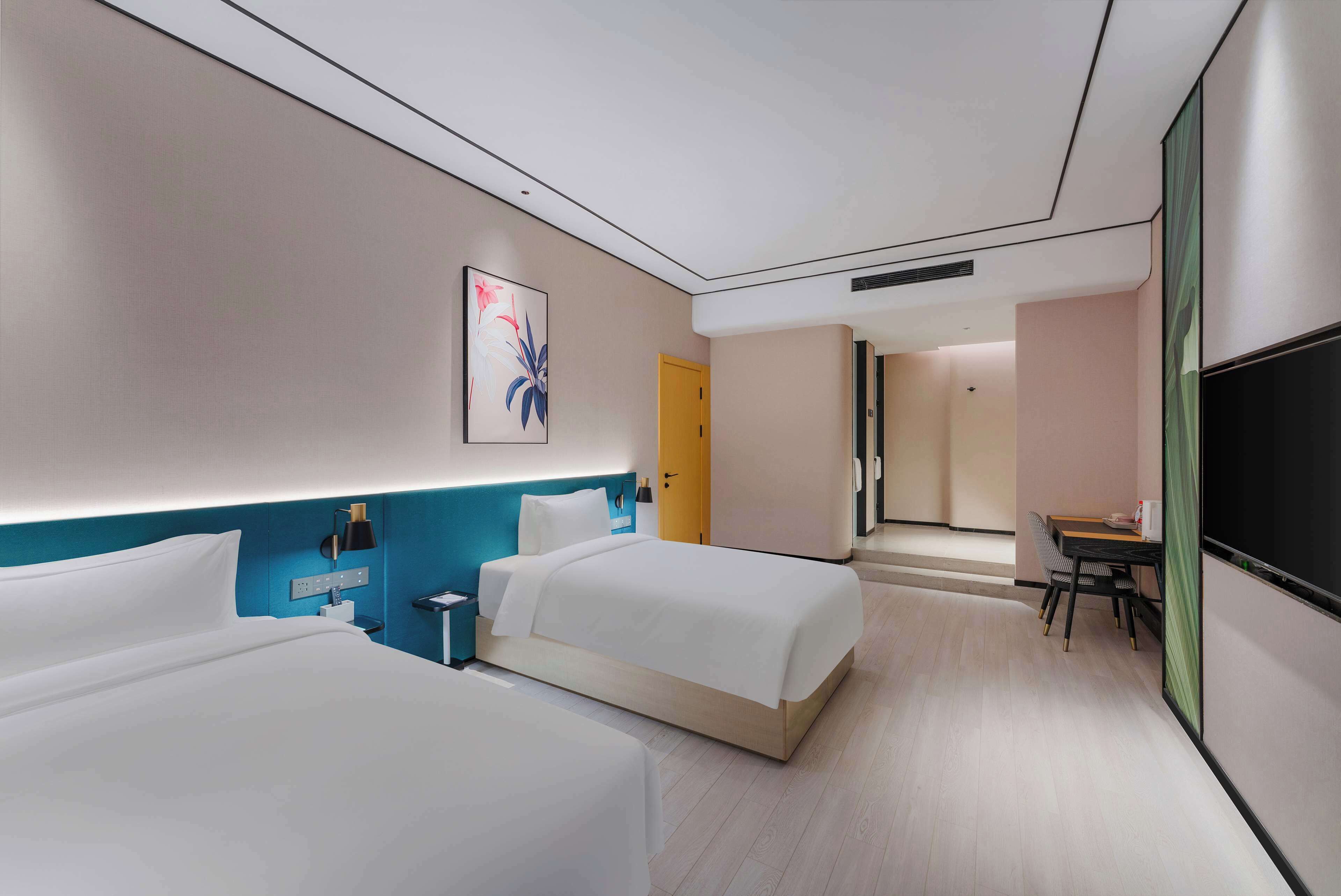 Habitación de hotel con dos camas, un escritorio, una silla, un televisor y una puerta que da a otra habitación.