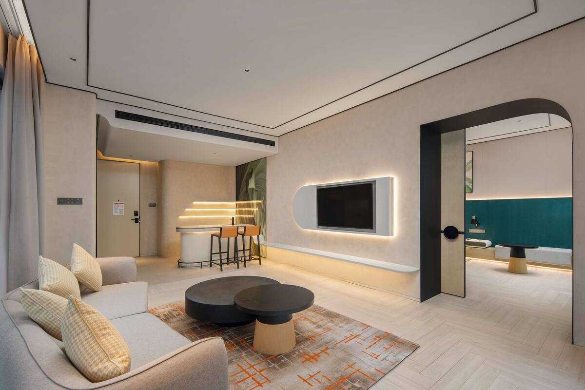 Un salon moderne avec un canapé, deux tables rondes, un téléviseur fixé au mur et un espace piscine visible à travers une arche.