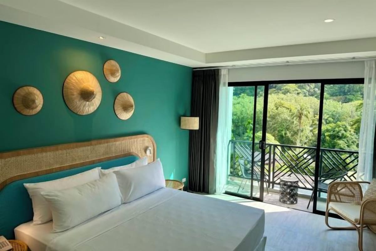 A hotel room with a large bed, a balcony with a view of greenery, and a wicker headboard.