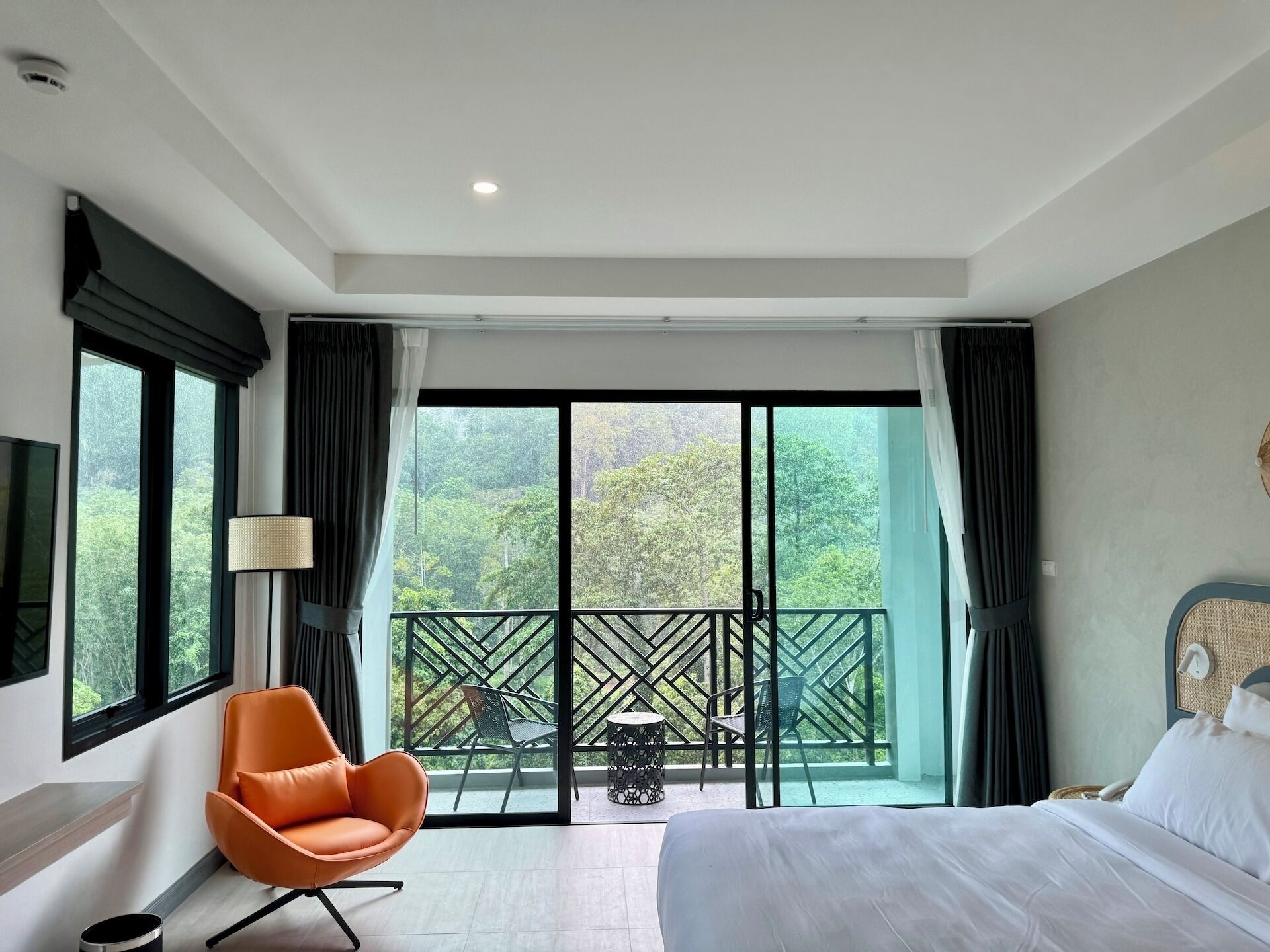 Une chambre d’hôtel avec un lit, un fauteuil orange, une table et un balcon donnant sur un paysage verdoyant.