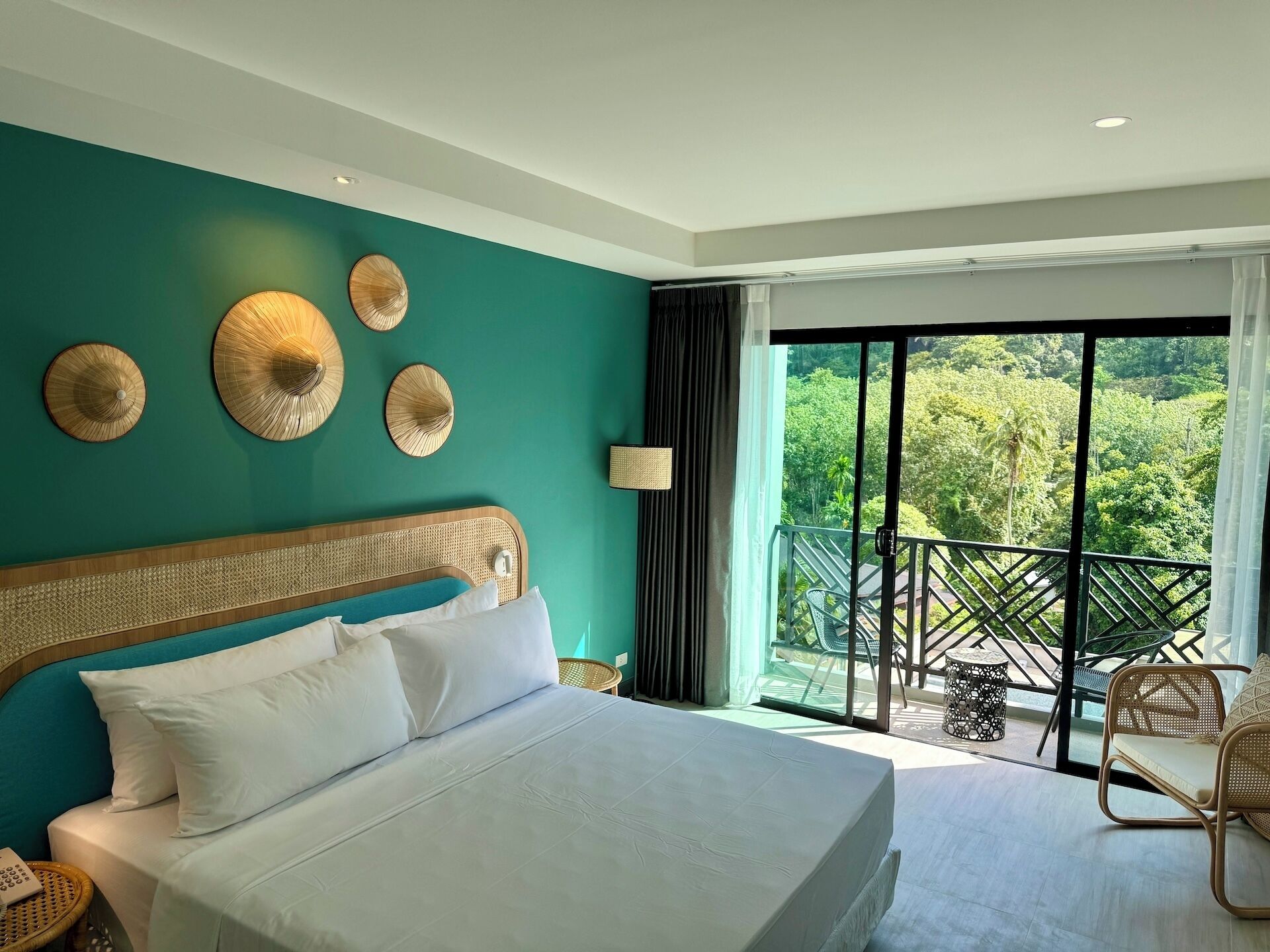 Une chambre d’hôtel avec un grand lit, une vue sur la verdure depuis le balcon et un plafond doté d’un éclairage encastré.