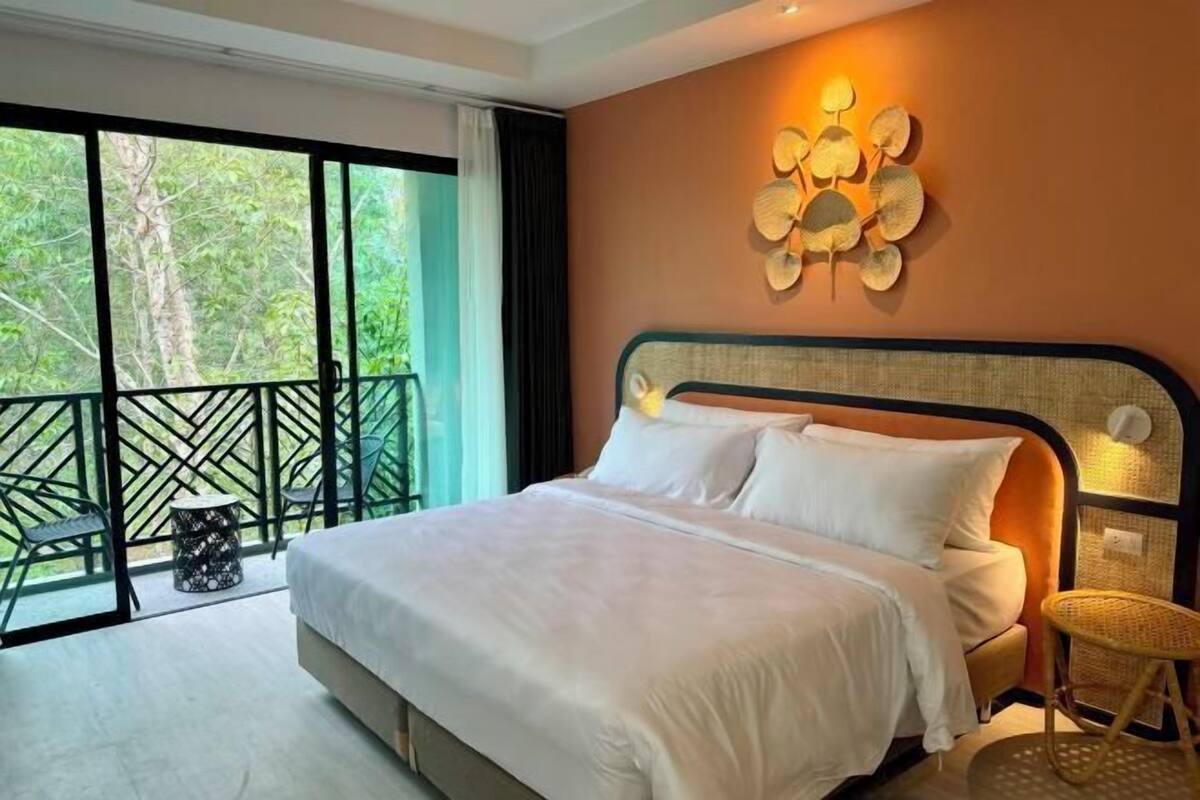 A bedroom with a bed, a balcony with chairs, and a wall-mounted decorative piece.