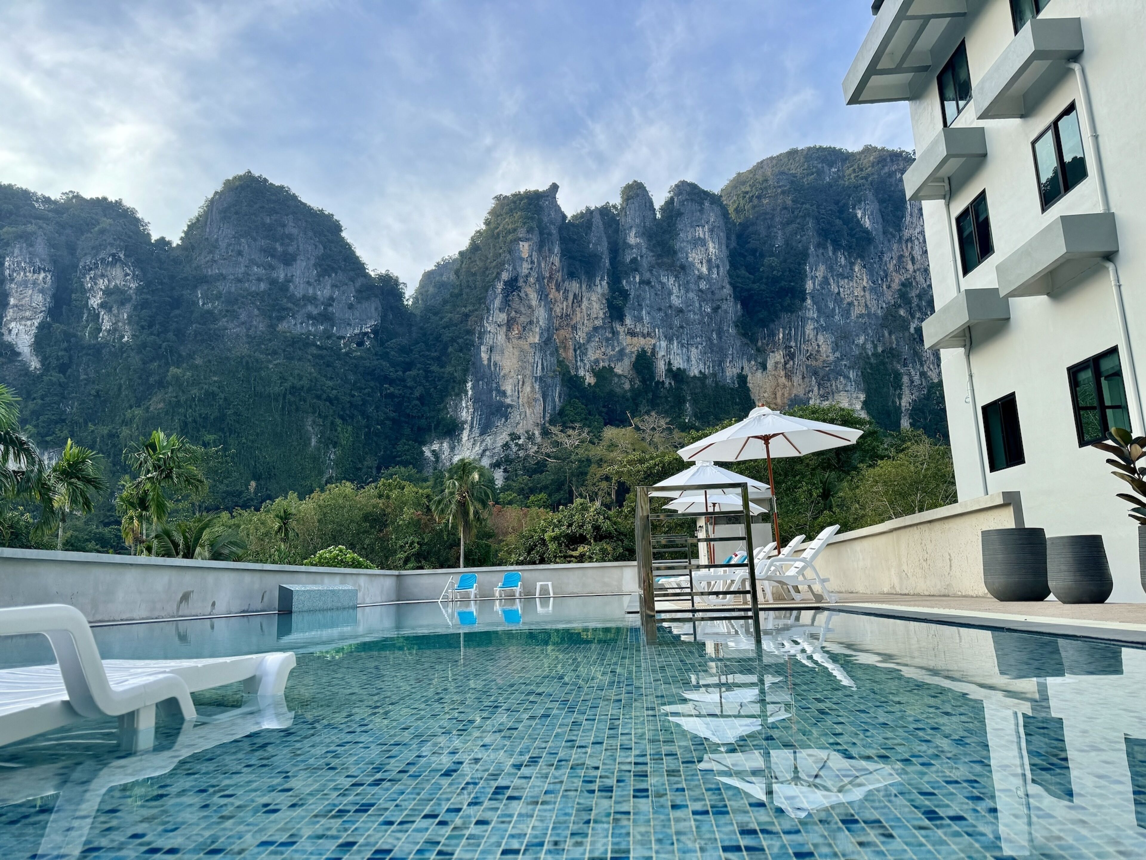 Une piscine entourée de chaises longues et de parasols, avec en arrière-plan des falaises rocheuses et une végétation luxuriante.