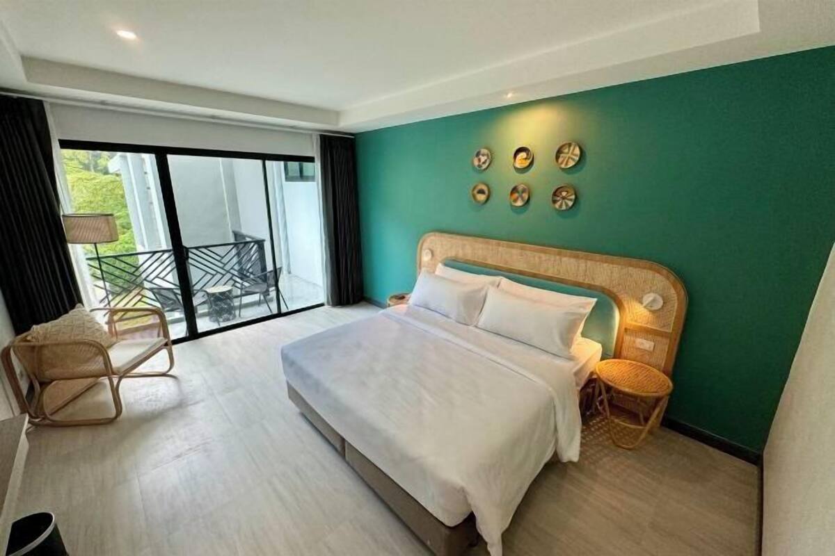 A bedroom with a large bed, a balcony with a chair, and a view of greenery.