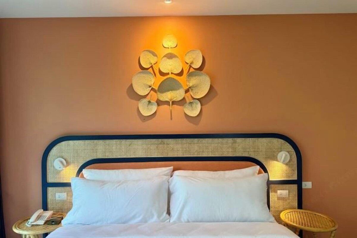 A bed with white linens, a headboard with a woven texture, and a wall-mounted light fixture.