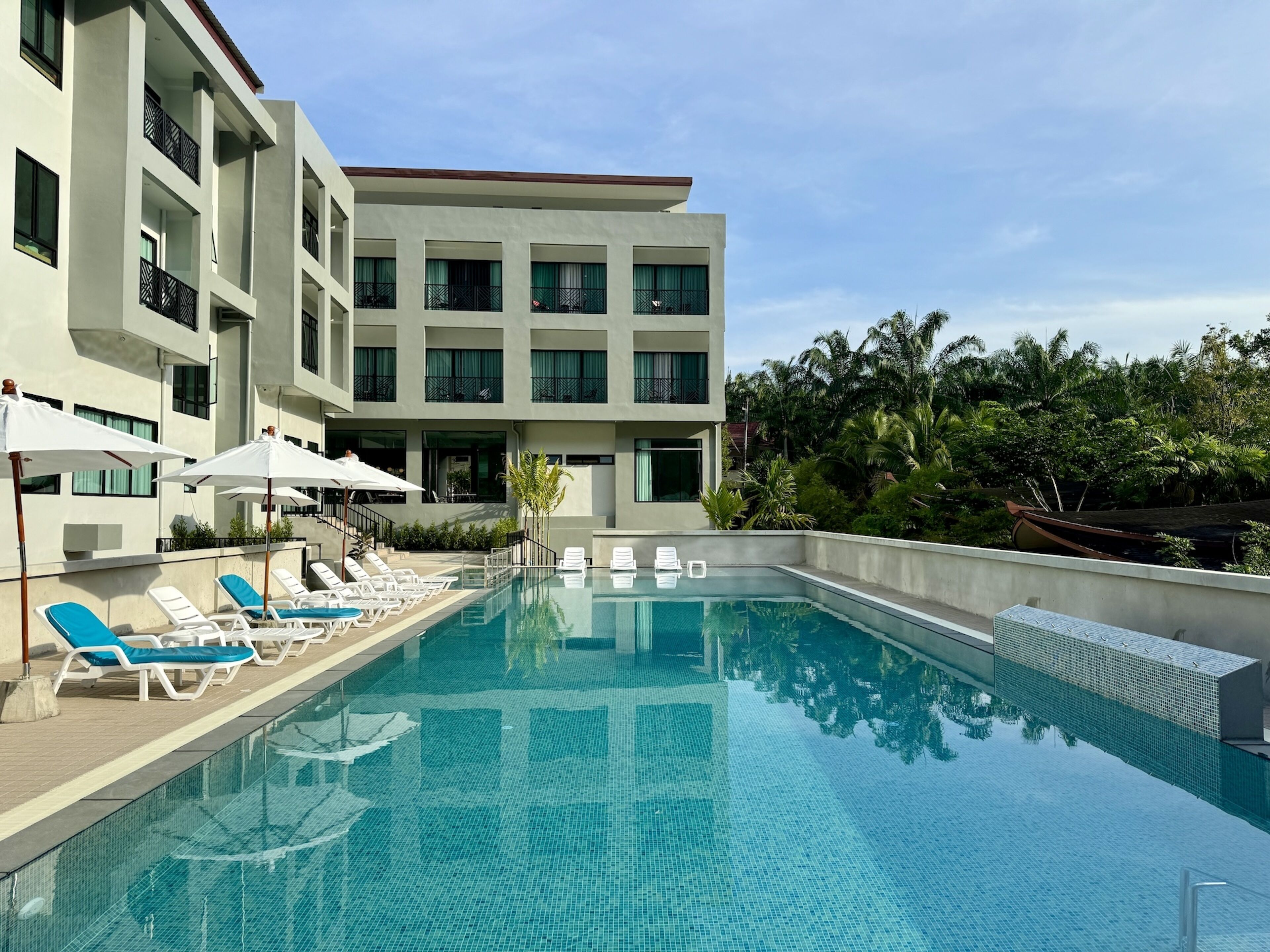 Um hotel moderno com piscina, espreguiçadeiras e vista para o verde ao redor.