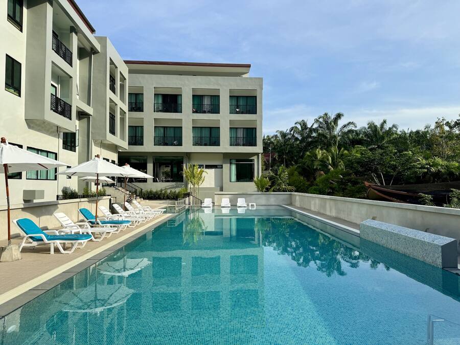Um hotel moderno com piscina, espreguiçadeiras e vista para o verde ao redor.