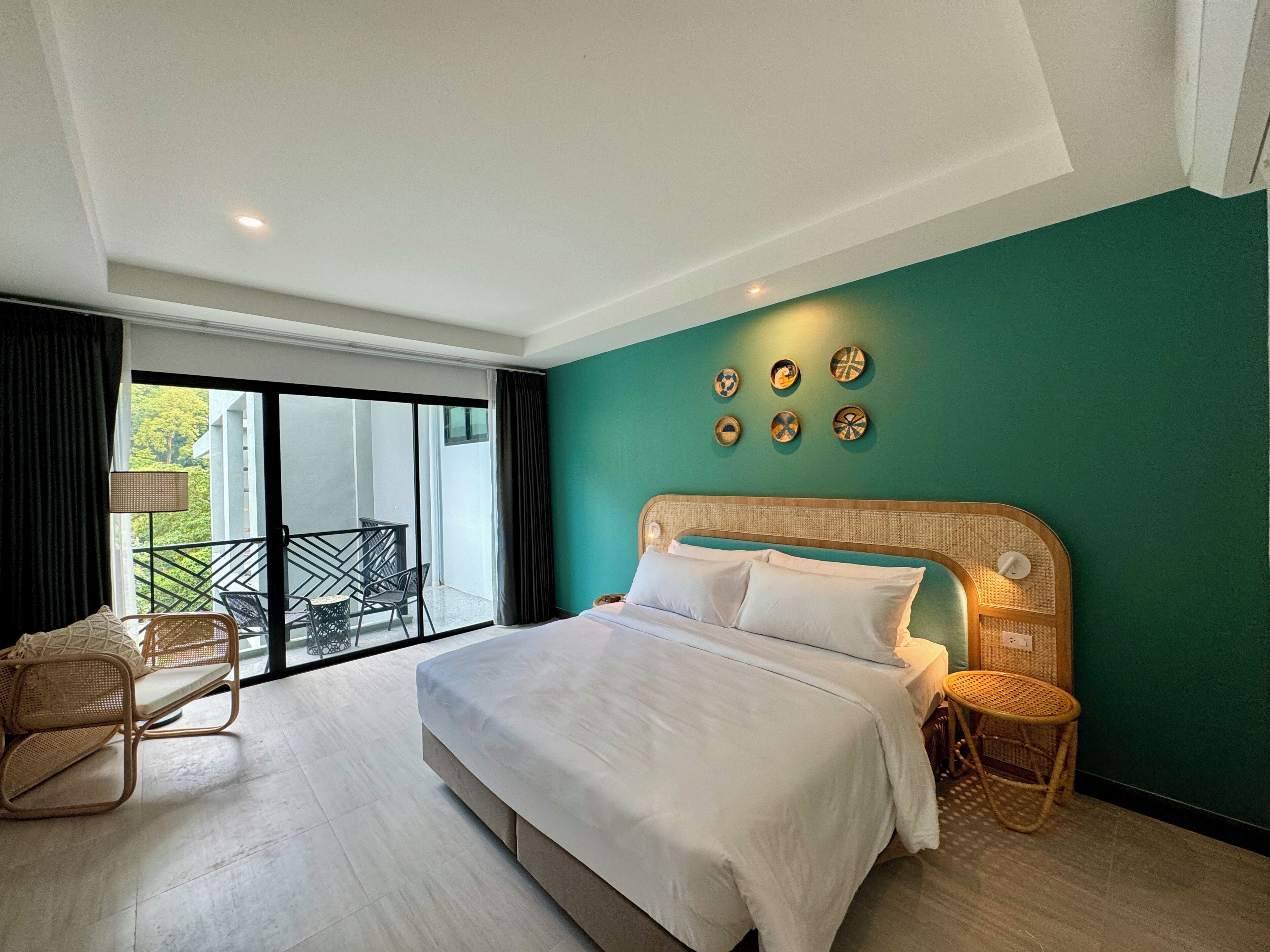 Une chambre d’hôtel moderne avec un grand lit, un balcon offrant une belle vue et un mur d’accent vert.