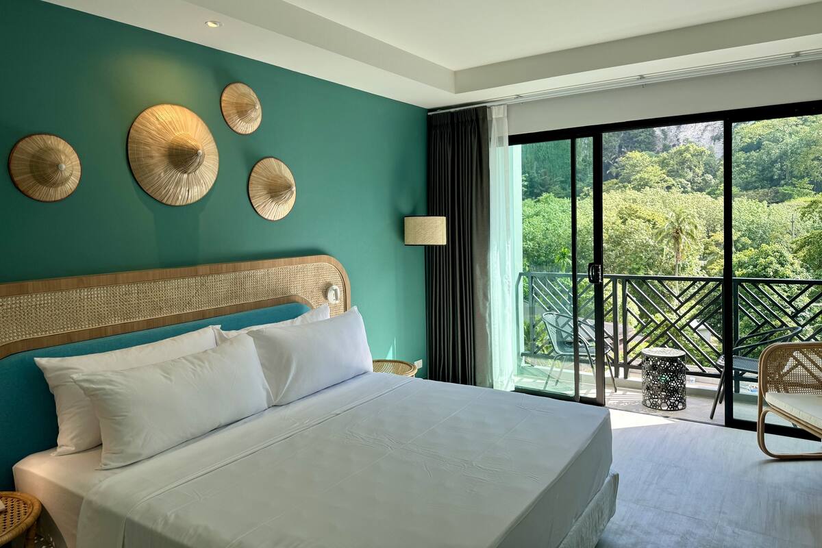 A bedroom with a large bed, a view of lush greenery through a balcony, and decorative wall art.
